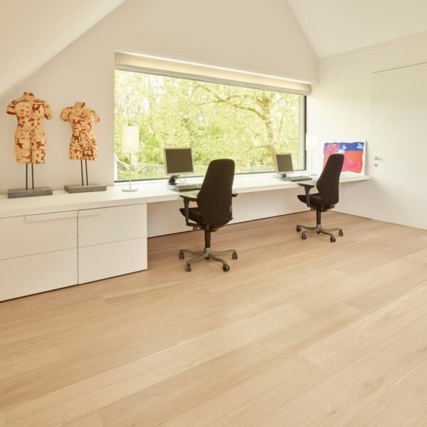 Bureau minimaliste aménagé sous les combles. Long plan de travail blanc pour deux postes, grande fenêtre donnant sur les arbres. Plancher bois clair.