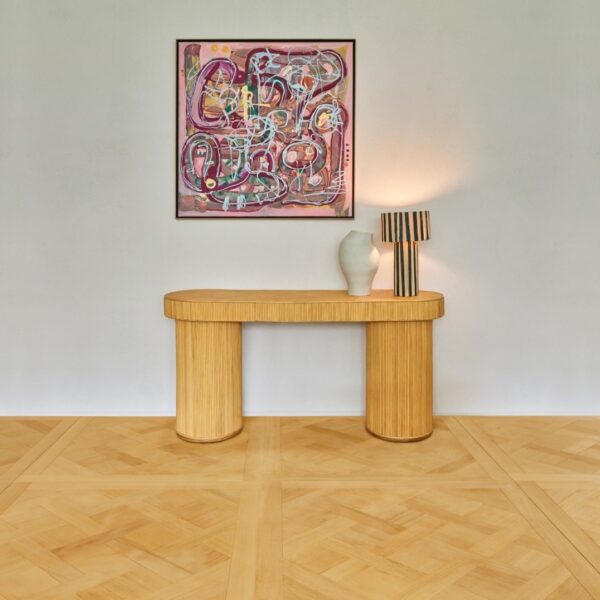 Console bois et lampe rayée, sous un tableau abstrait rose audacieux. Un vase design repose sur la table. Parquet à motifs clairs.
