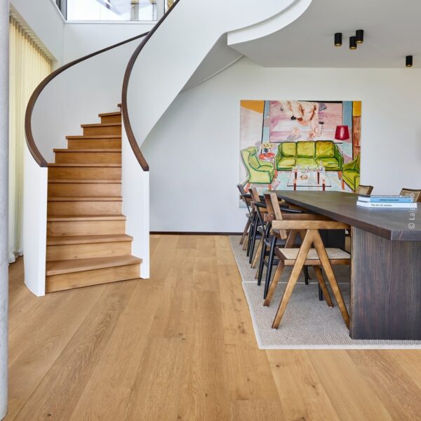 Escalier sculptural courbe en chêne clair et blanc. Salle à manger contemporaine avec table foncée, chaises design et grand tableau d'art figuratif.