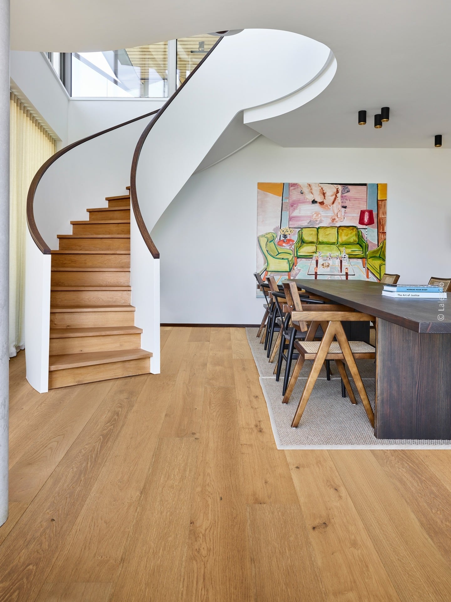 Escalier sculptural courbe en chêne clair et blanc. Salle à manger contemporaine avec table foncée, chaises design et grand tableau d'art figuratif.