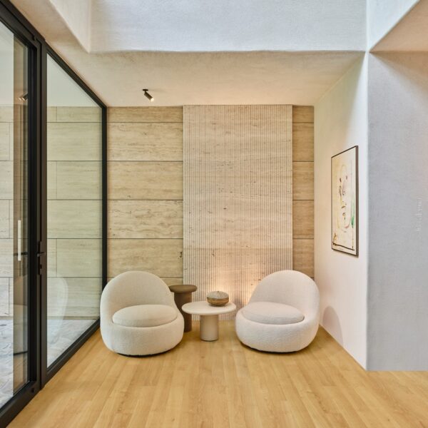 Coin salon moderne: deux fauteuils bouclette moelleux, tables rondes, murs texturés et revêtement en travertin nervuré.