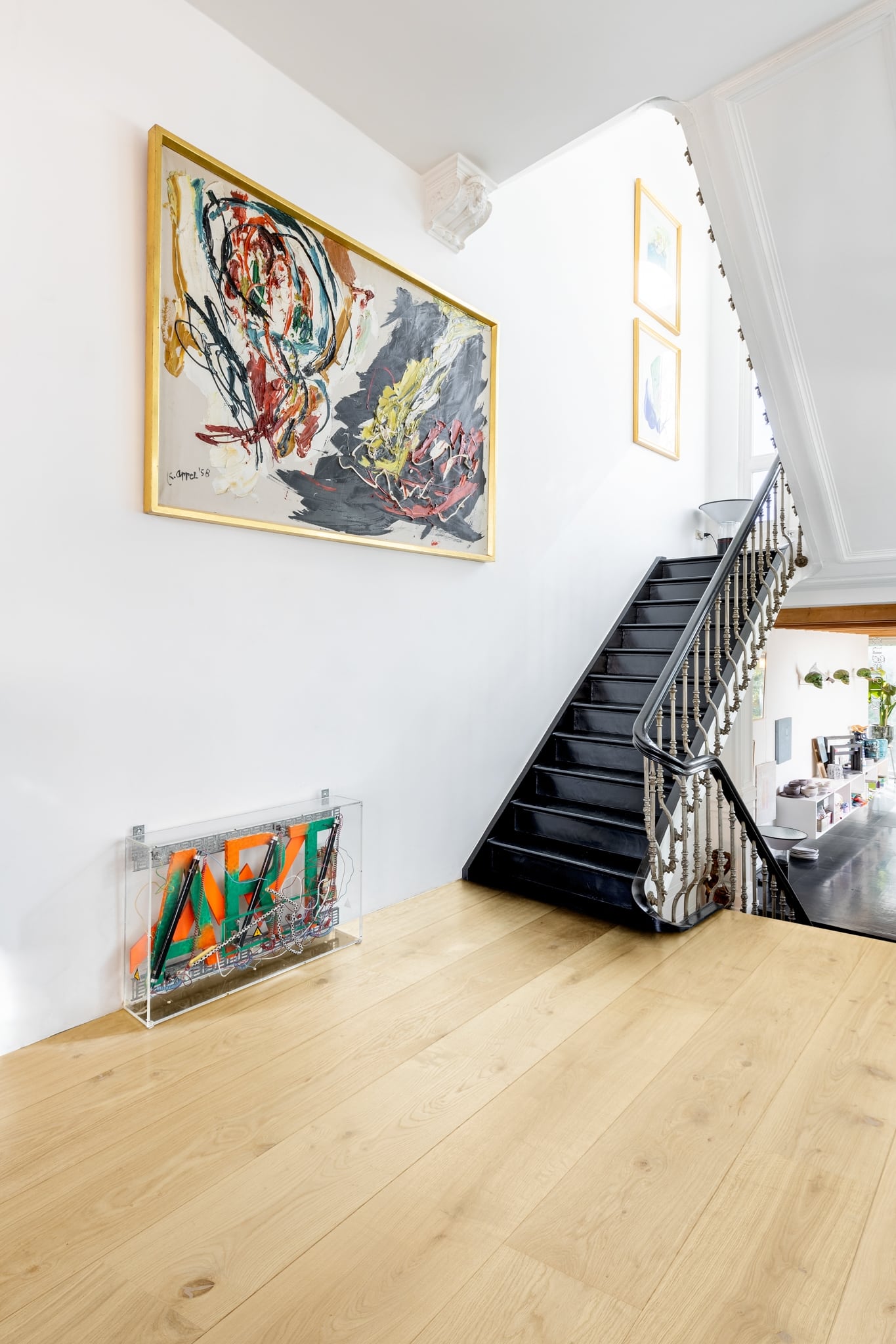 Hall d'entrée lumineux avec parquet clair et escalier noir. Grande toile abstraite signée K. Appel '58 au-dessus d'une sculpture cinétique.