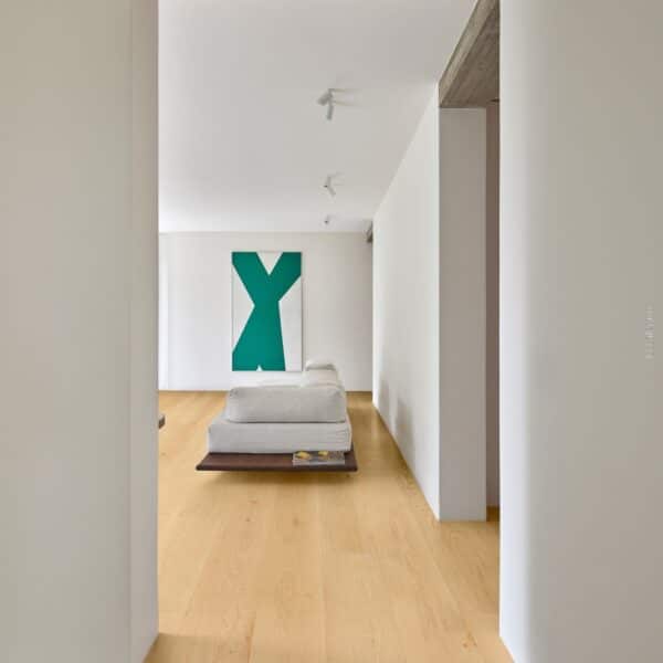 Intérieur design minimaliste, plancher bois chêne, poutre béton brut. Canapé blanc face au tableau abstrait vert (© Lalegno).
