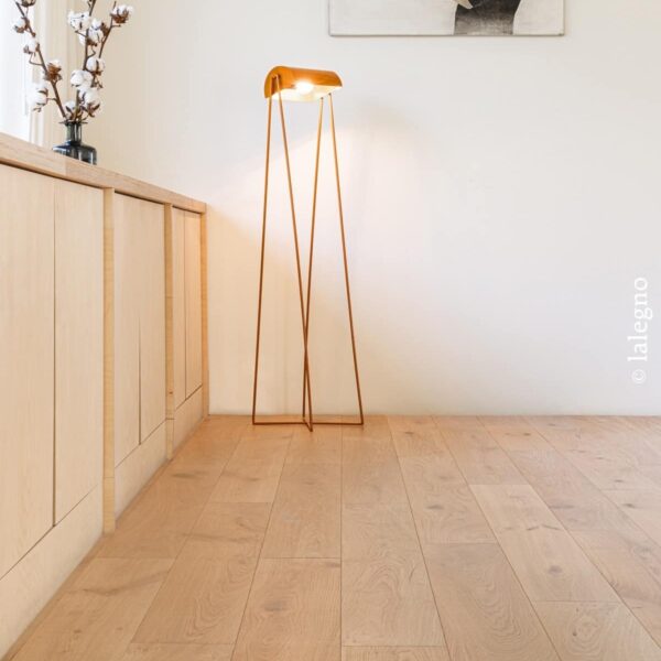 Parquet chêne naturel Lalegno. Long meuble en bois clair, lampe minimaliste cuivre et branches de coton pour un intérieur moderne.