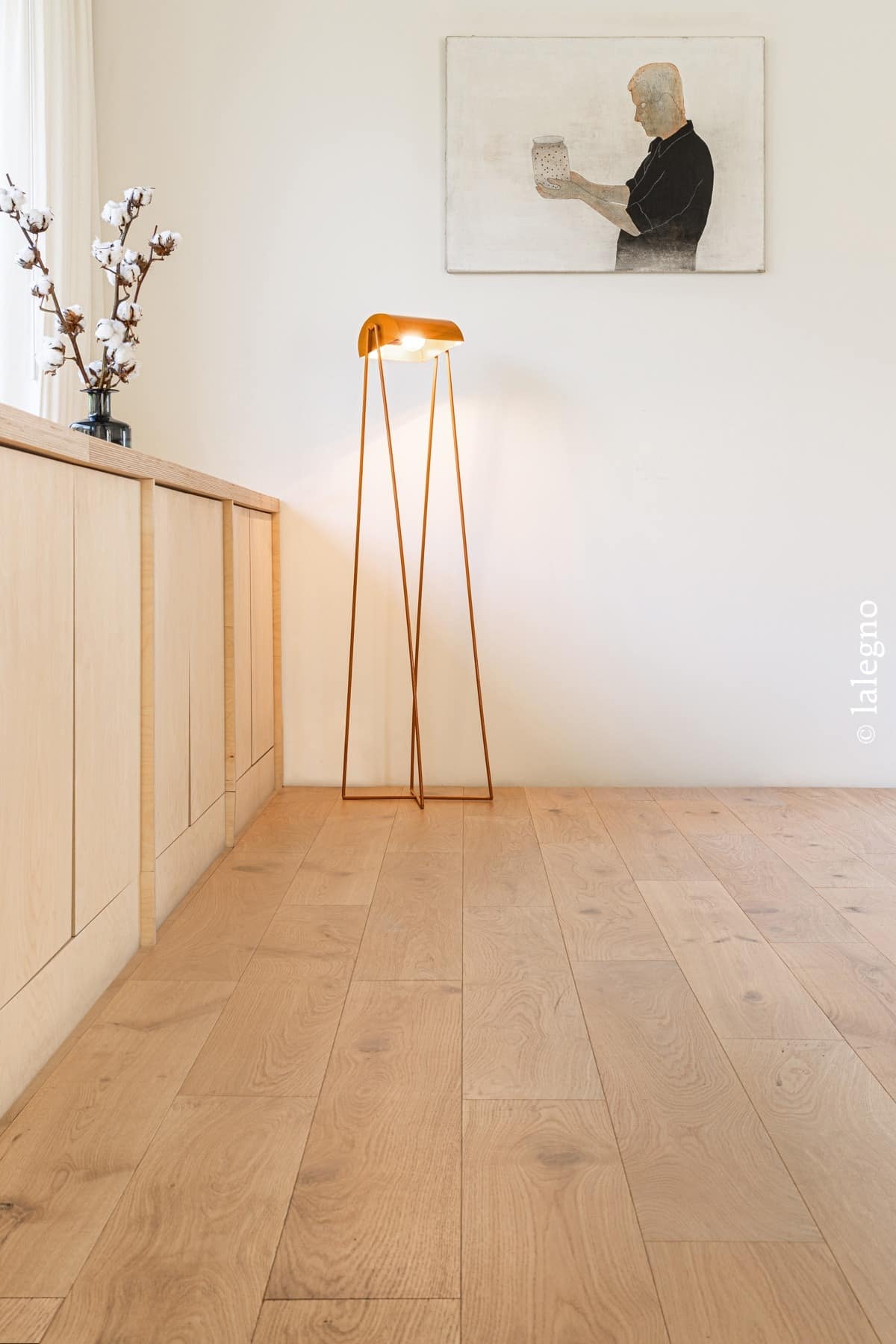 Parquet chêne naturel Lalegno. Long meuble en bois clair, lampe minimaliste cuivre et branches de coton pour un intérieur moderne.