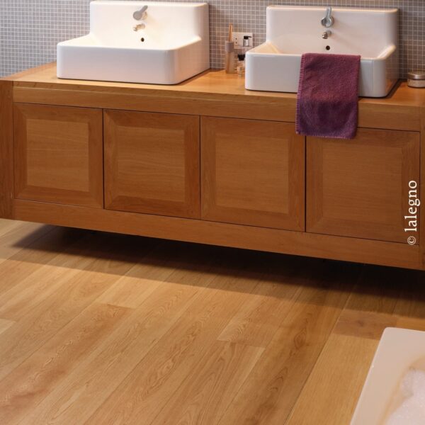 Meuble double vasque flottant en bois clair (chêne) surmonté de deux lavabos blancs. Parquet en chêne. Mosaïque grise.