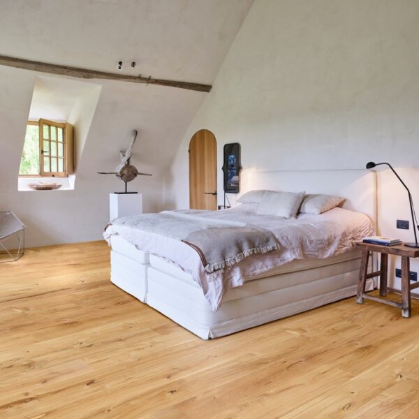 Chambre rustique chic sous les toits: grand lit, parquet chêne naturel, poutre brute, porte en bois arrondie et sculpture sur socle.