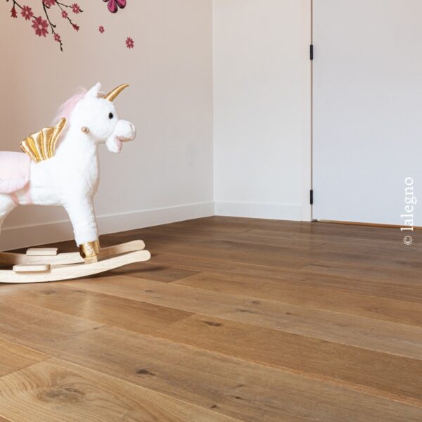 Parquet chêne clair, finition miel, dans une chambre d'enfant. Licorne à bascule blanche et décoration murale fleurie rose.