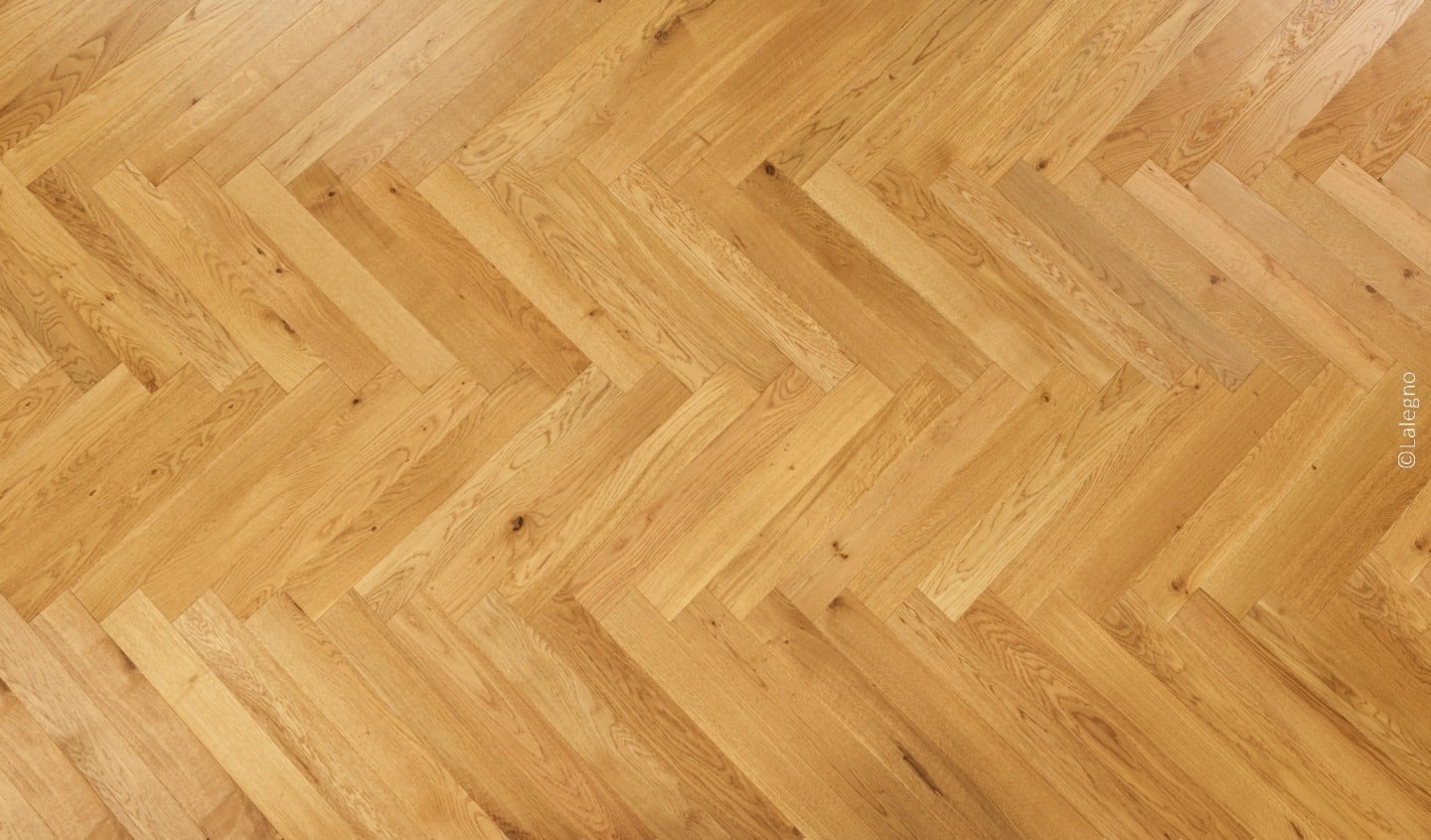 Parquet de chêne naturel clair posé en chevron. Motif géométrique en V. Texture bois avec grain visible. (Watermark: ©Lalegno).