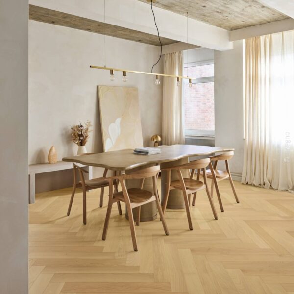 Parquet chêne clair à chevrons dans une salle à manger industrielle chic. Table en bois organique, lustre laiton et plafond béton.