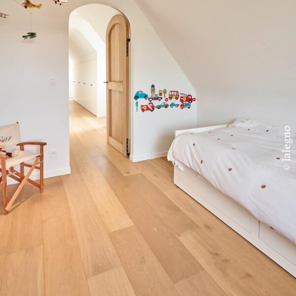 Parquet en chêne clair large lame dans une chambre d'enfant mansardée. Porte en bois cintrée, lit blanc et chaise "César".