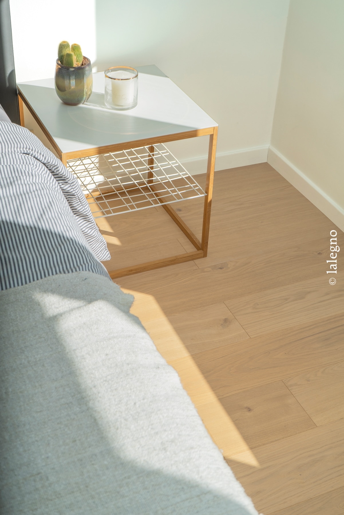 Parquet chêne clair naturel dans une chambre minimaliste baignée de soleil, avec table de chevet et cactus.