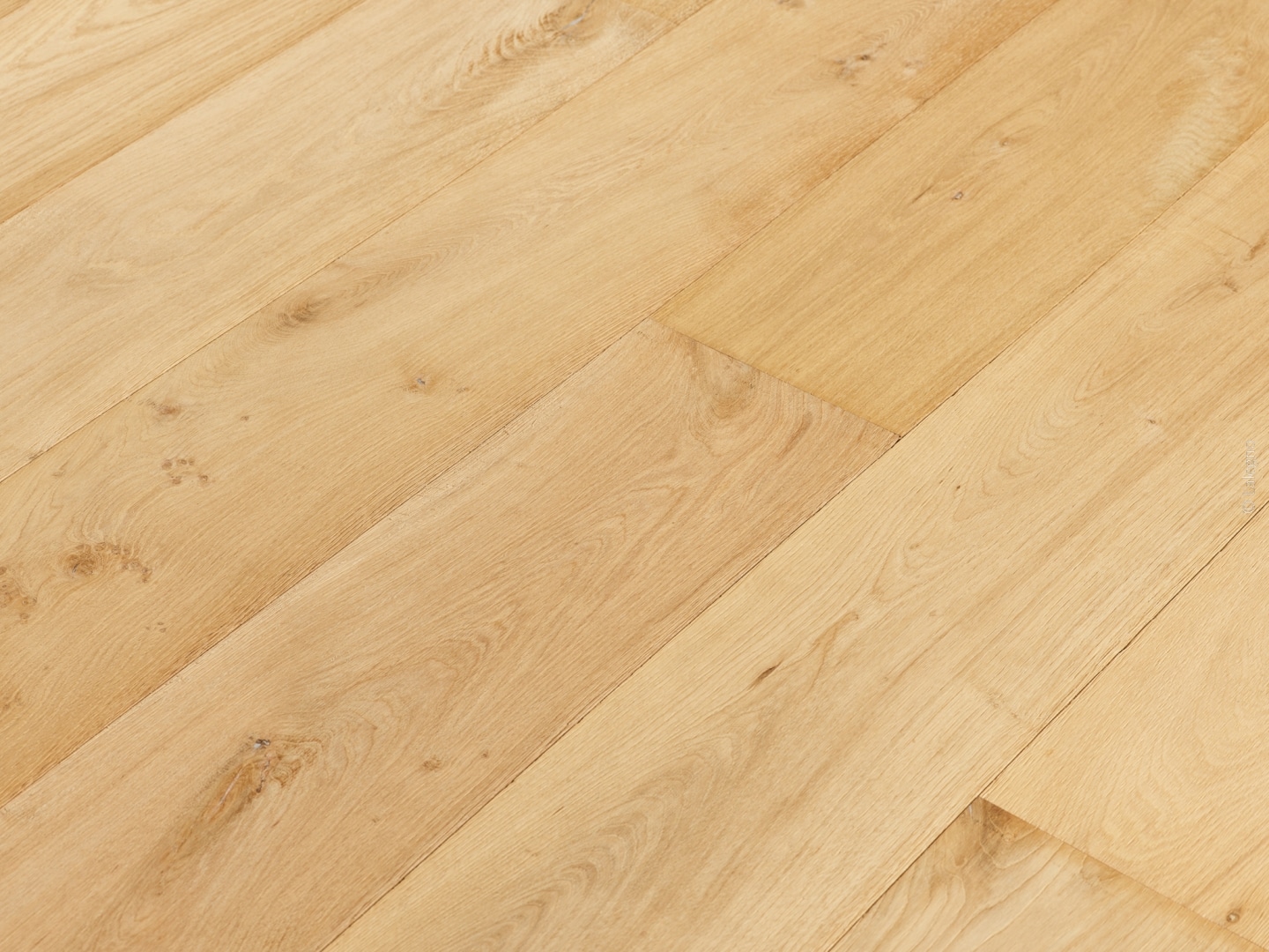 Gros plan d'un parquet en chêne clair posé en chevron. Lames larges avec grain naturel et finition mate.