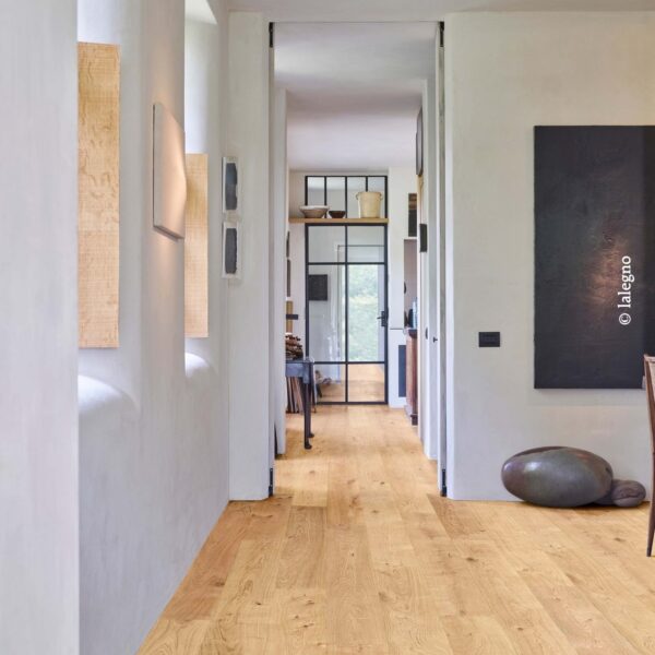 Parquet chêne clair dans couloir lumineux aux murs blancs. Porte vitrée noire, décor minimaliste et œuvre d'art noire.