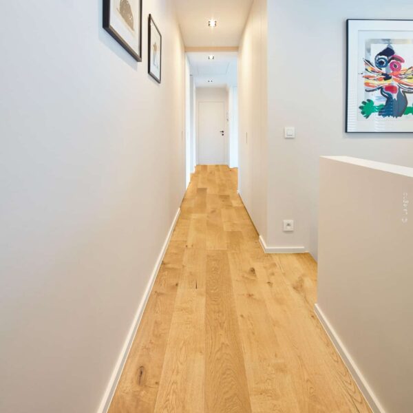 Couloir moderne et lumineux. Parquet en chêne, murs blancs, et un tableau d'art moderne coloré contrastant avec des œuvres sobres.