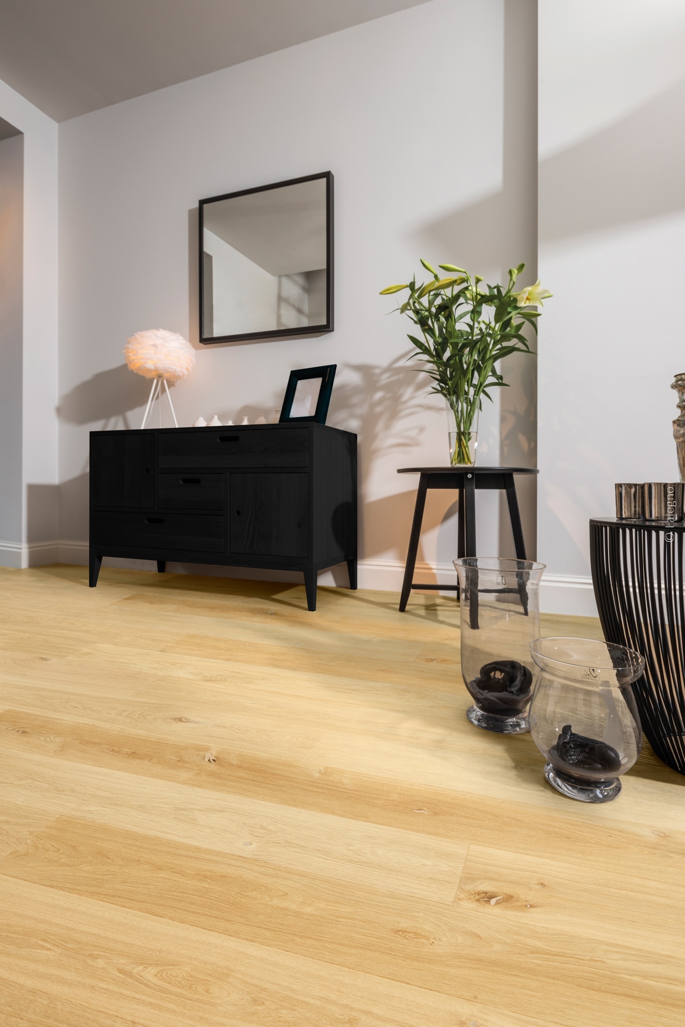 Parquet chêne clair naturel, posé dans une entrée moderne. Le sol chaud contraste avec le mobilier noir ébène et les murs gris.