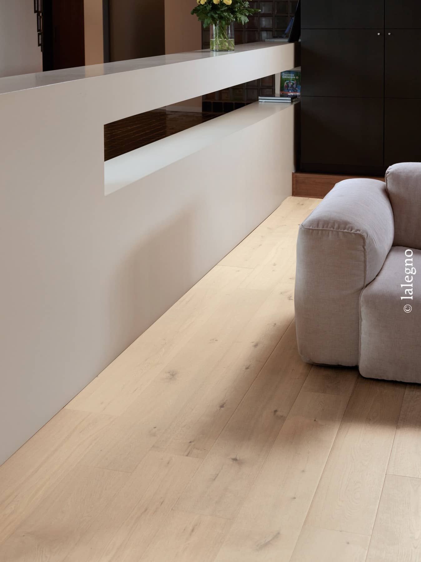 Plancher chêne clair large lame dans un salon moderne avec un canapé modulaire beige, un comptoir blanc et des armoires noires. © lalegno.