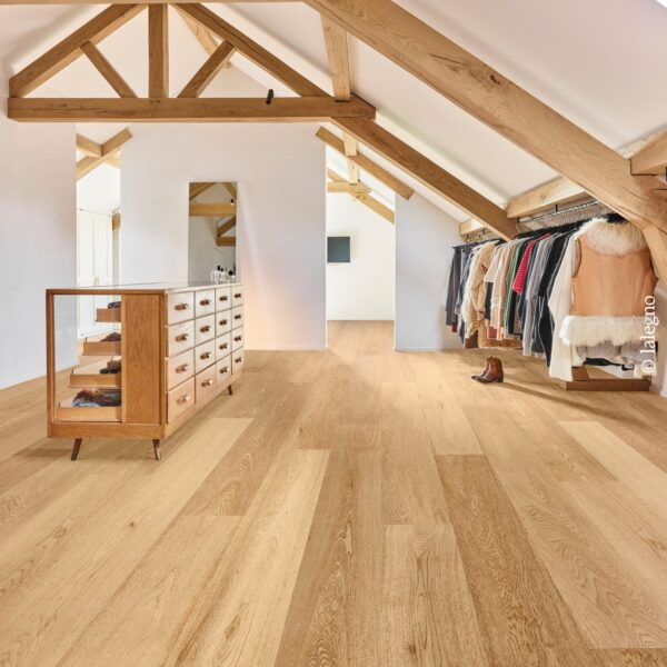 Dressing lumineux sous combles. Parquet chêne clair, charpente en bois massif et murs blancs. Une commode vintage fait face à un portant à vêtements.