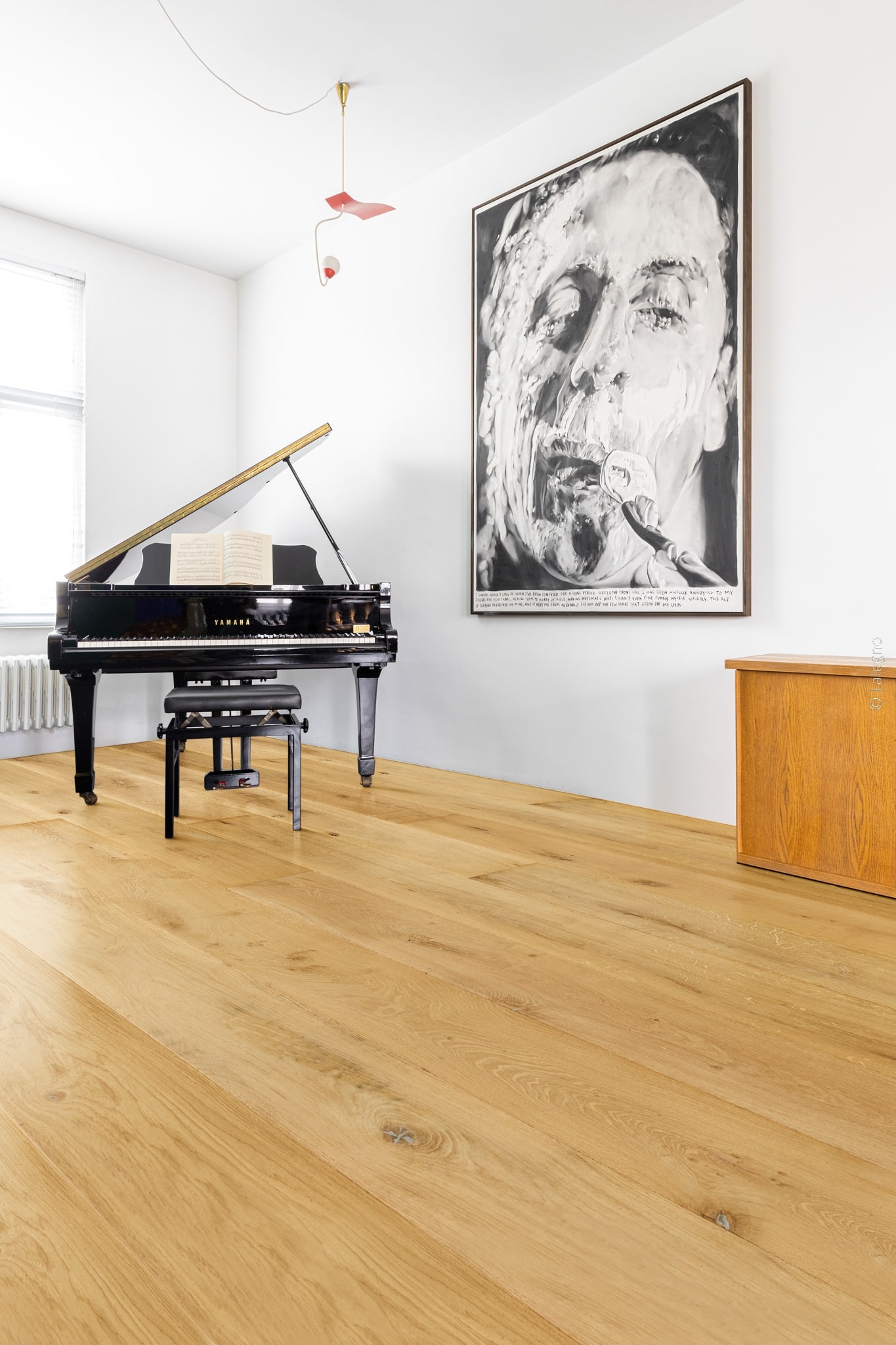 Grand piano à queue Yamaha noir dans un salon minimaliste. Parquet de chêne clair et œuvre d'art portrait noir et blanc imposante.