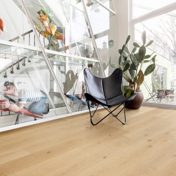 Parquet chêne clair dans un intérieur lumineux. Verrière architecturale exposant des statues de Pinocchio et Popeye. Fauteuil papillon et cactus.