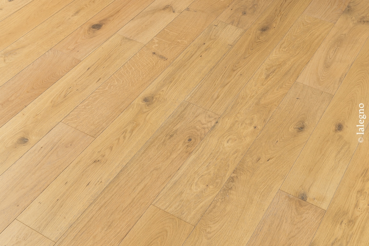 Parquet en chêne clair posé en lames larges et diagonales. Le sol présente des nœuds naturels et une couleur bois doré.