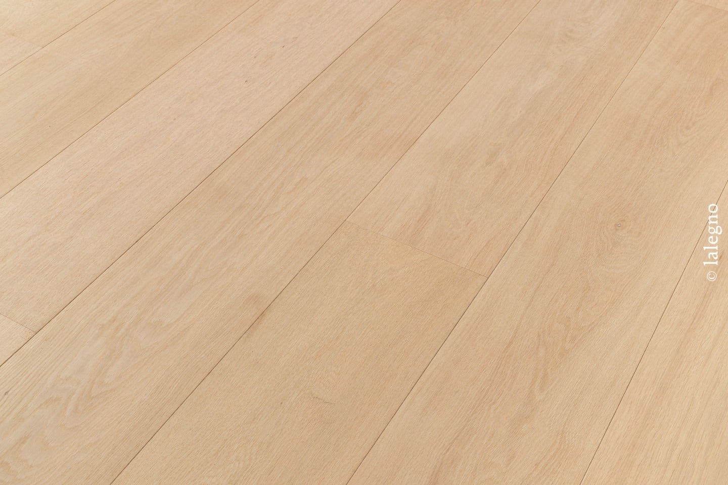 Gros plan sur un revêtement de sol en parquet chêne clair à lames larges, bois blond naturel, pose diagonale.