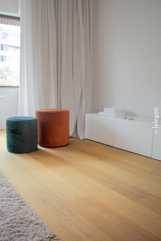 Plancher chêne clair. Deux poufs velours orange et turquoise devant rideaux blancs. Meuble bas blanc. Décoration moderne et lumineuse. © lalegno.