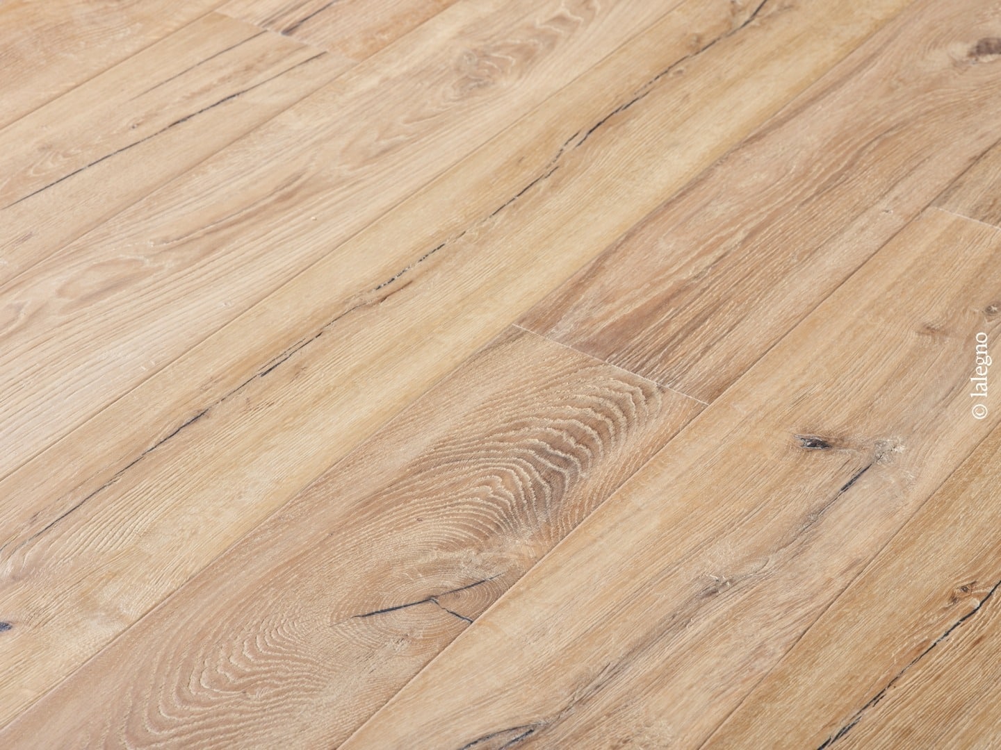 Gros plan sur un parquet en bois clair, lames rustiques avec grain et fissures noires, posé en diagonale. © lalegno.