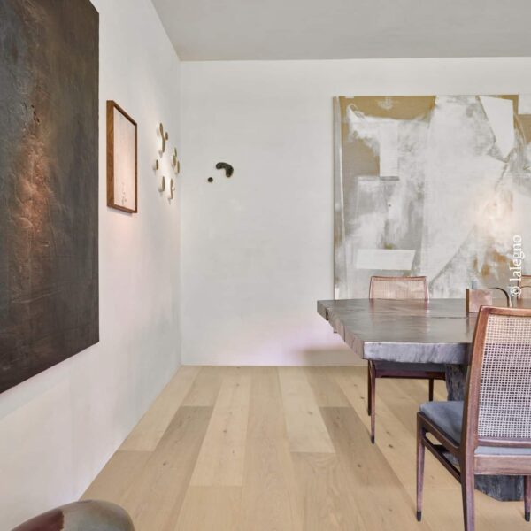 Parquet chêne clair naturel Lalegno dans salle à manger minimaliste. Table en bois brut, chaises cannées et grands tableaux d'art abstrait.