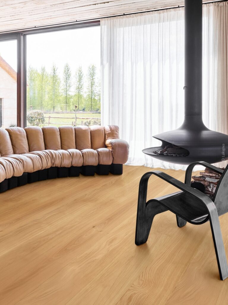Parquet bois clair pour un salon design et moderne. Parquet chêne clair dans un salon moderne. Canapé modulaire, fauteuil noir et foyer suspendu design. Vue sur la nature. © Lalegno.