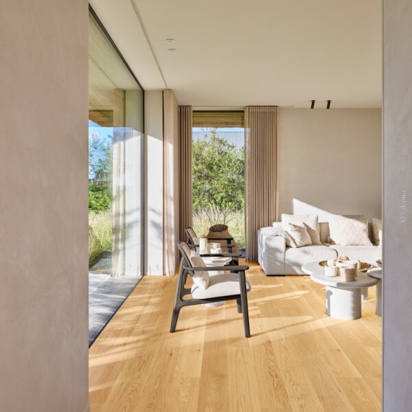 Salon lumineux, parquet chêne clair. Sofa neutre, fauteuils design noir, baie vitrée sur jardin luxuriant. Murs texturés clairs.