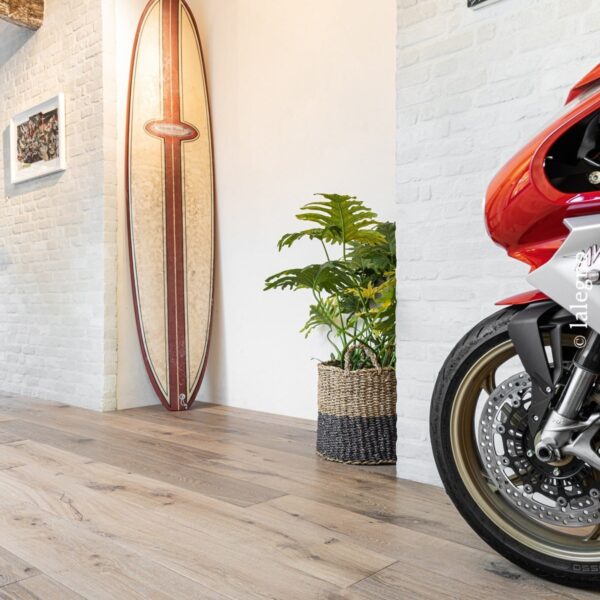 Plancher chêne clair. Décoration design industriel avec mur brique blanc, surf vintage, grande plante verte et roue avant de moto rouge.