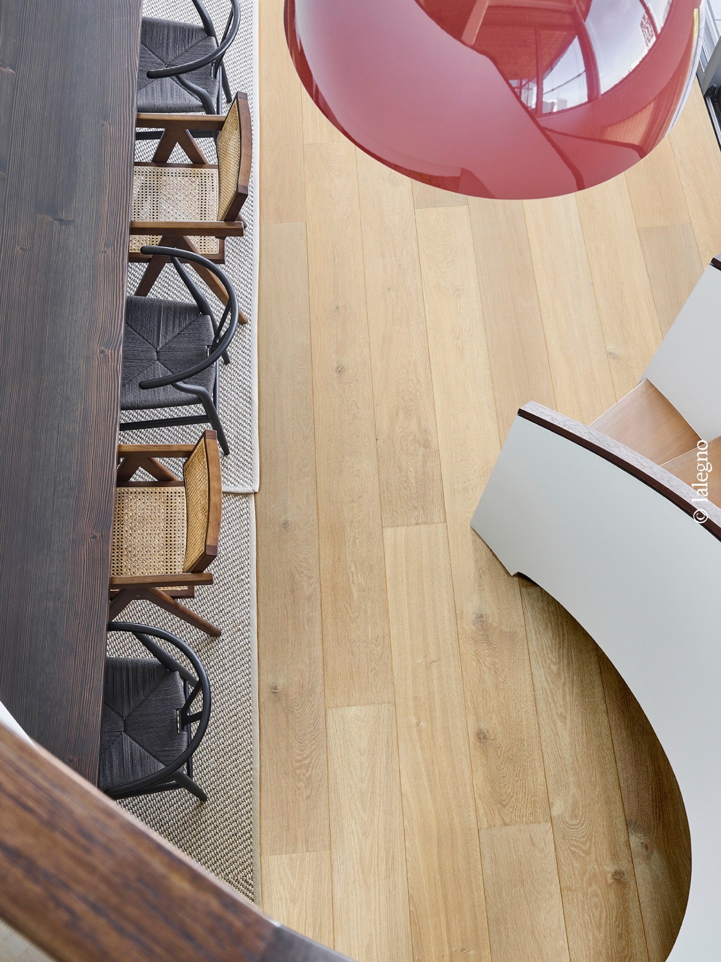 Parquet chêne clair, table en bois brûlé sombre et mélange de chaises en cannage et tressé noir sur tapis. Vue intérieure moderne.