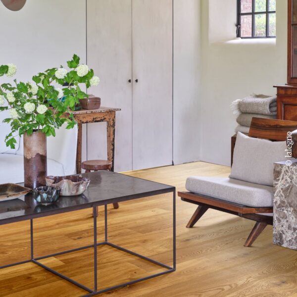 Parquet en chêne doré dans un salon rustique chic. Table basse en métal, fauteuil en bois, armoires patinées et fenêtre ancienne.