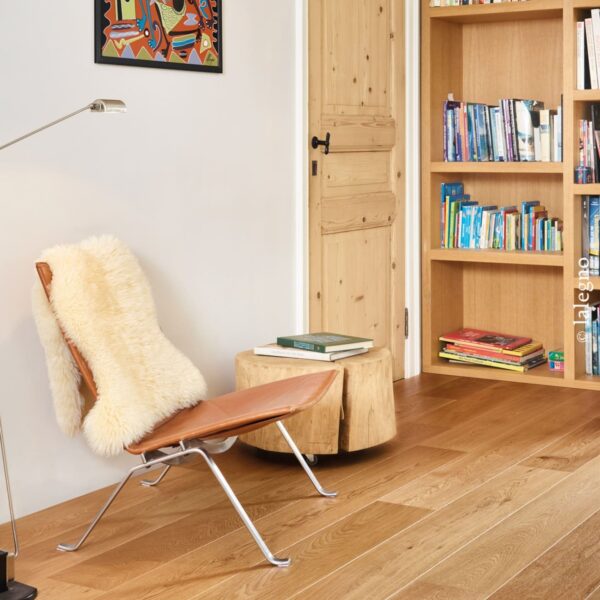 Coin lecture confortable : fauteuil papillon en cuir, table en rondins, lampadaire moderne. Parquet en chêne clair, porte en pin et bibliothèque.