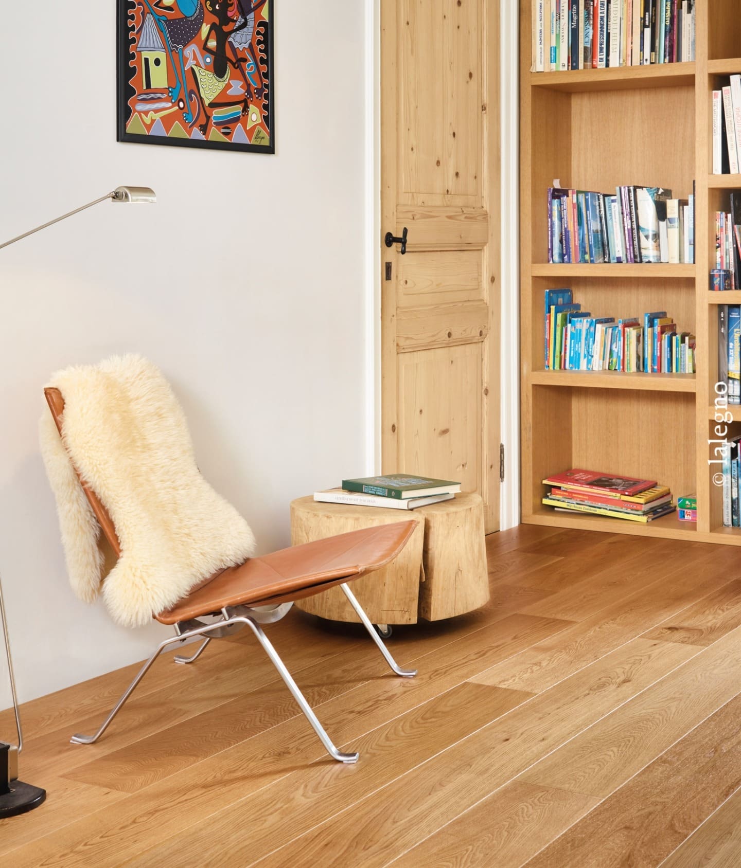 Coin lecture confortable : fauteuil papillon en cuir, table en rondins, lampadaire moderne. Parquet en chêne clair, porte en pin et bibliothèque.