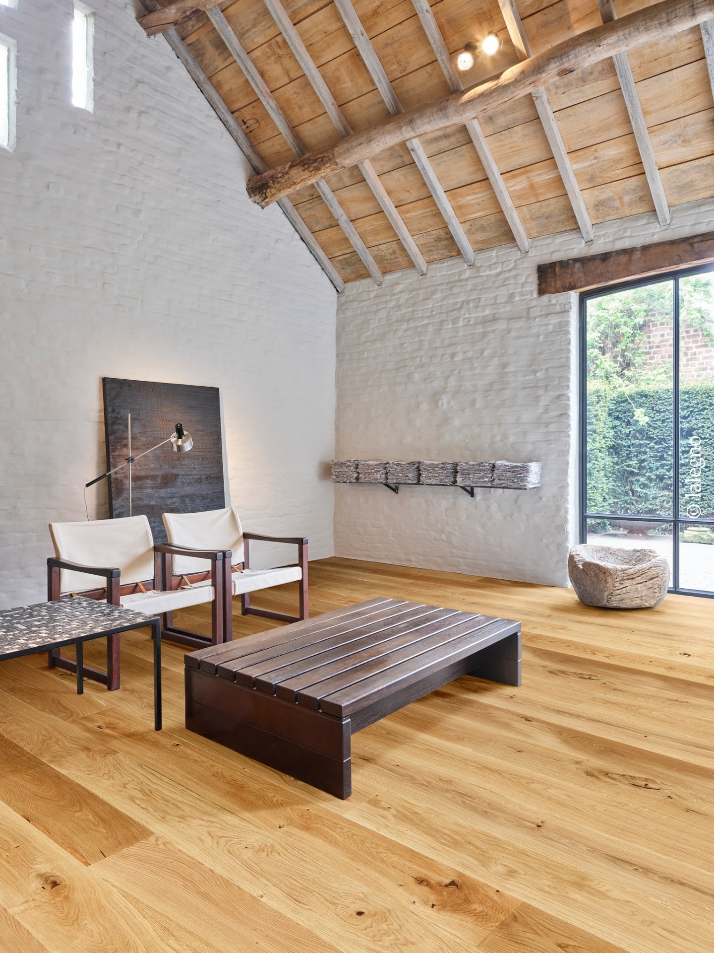 Loft design rustique aux murs de briques blanches et poutres apparentes. Parquet en chêne clair, mobilier sombre et baies vitrées.