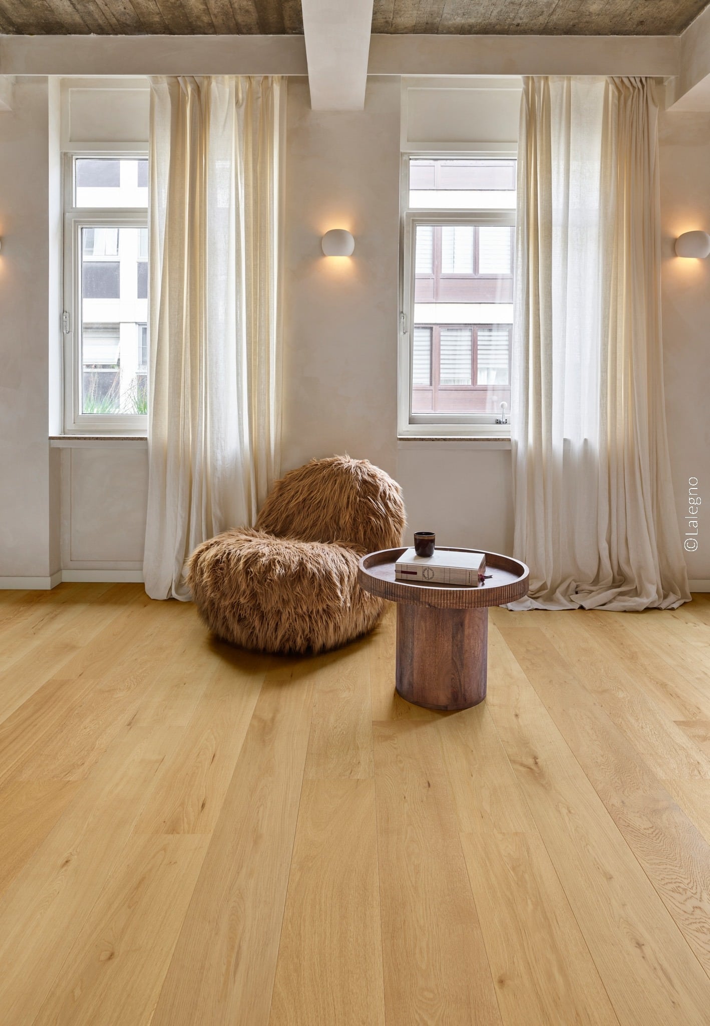 Parquet chêne naturel clair et fauteuil fourrure marron dans un intérieur style industriel. Lumière chaude et rideaux lin.