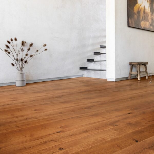 Parquet chêne brun chaud à planches larges dans un intérieur minimaliste. Mur blanc texturé, escalier flottant sombre et vase de chardons séchés.