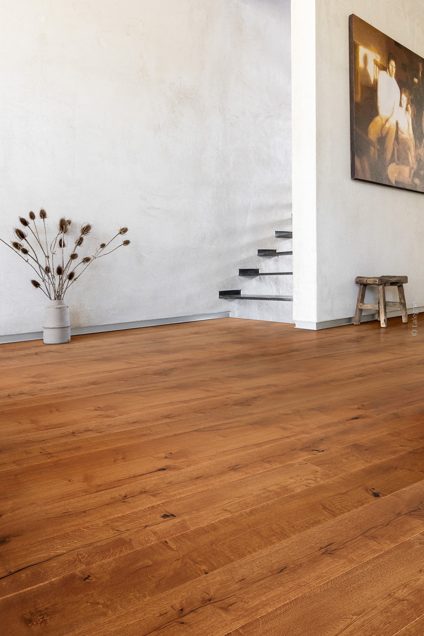 Parquet chêne brun chaud à planches larges dans un intérieur minimaliste. Mur blanc texturé, escalier flottant sombre et vase de chardons séchés.