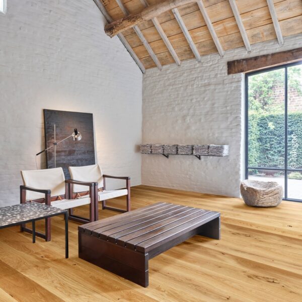 Intérieur lumineux de style rustique chic avec murs en briques blanches, plafond en poutres de bois et large parquet en chêne clair.