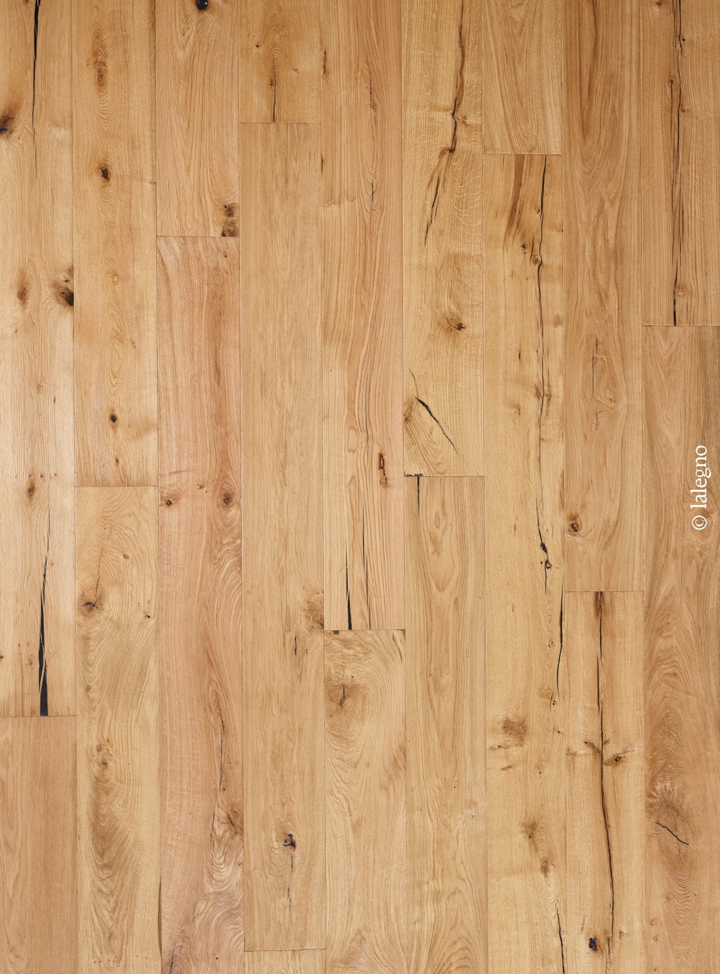 Parquet en chêne rustique naturel, lames verticales claires, présentant des nœuds et des fissures noires marquées. Copyright © lalegno.