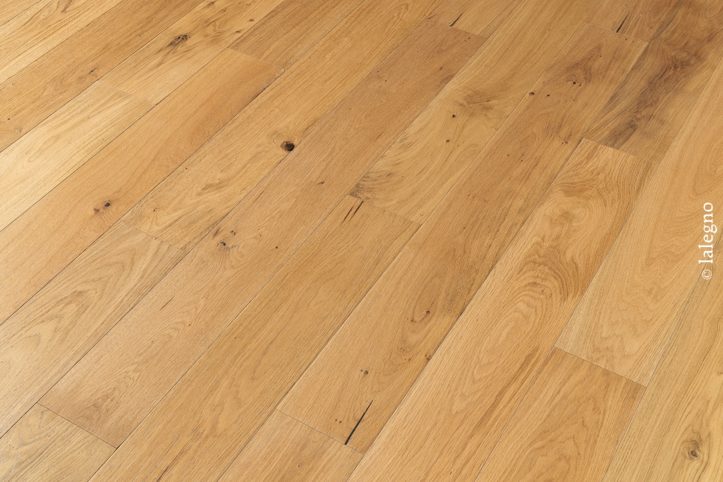 Parquet en chêne clair rustique à larges lames, montrant des nœuds et des fissures. Tonalité chaude.