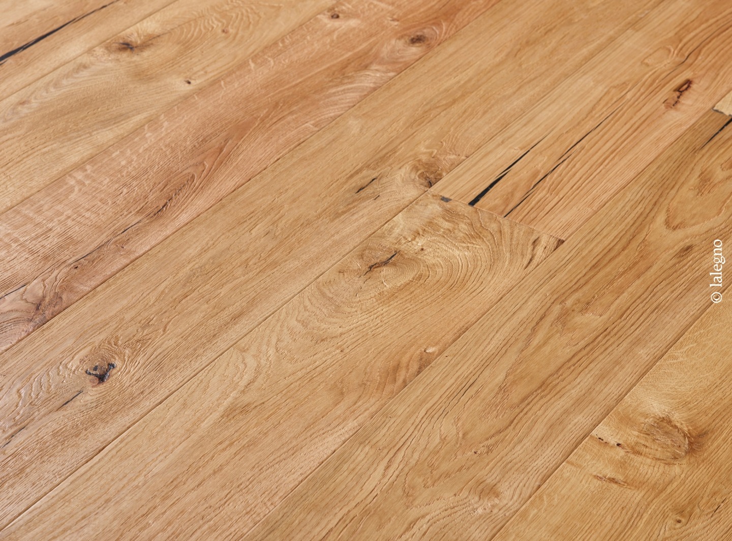 Parquet chêne rustique, lames larges en bois clair avec nœuds et fissures. Marque lalegno visible en bas à droite.