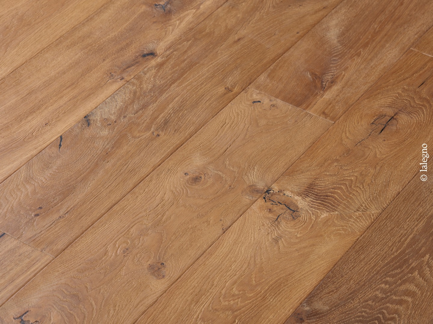 Parquet en chêne rustique posé en diagonale, couleur miel. La surface présente des nœuds noirs et des fissures.