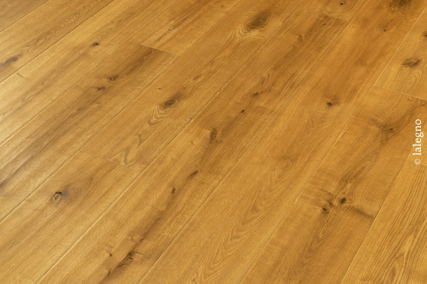 Parquet en chêne rustique, couleur miel doré, avec des nœuds visibles. Plancher à lames larges posées en diagonale.