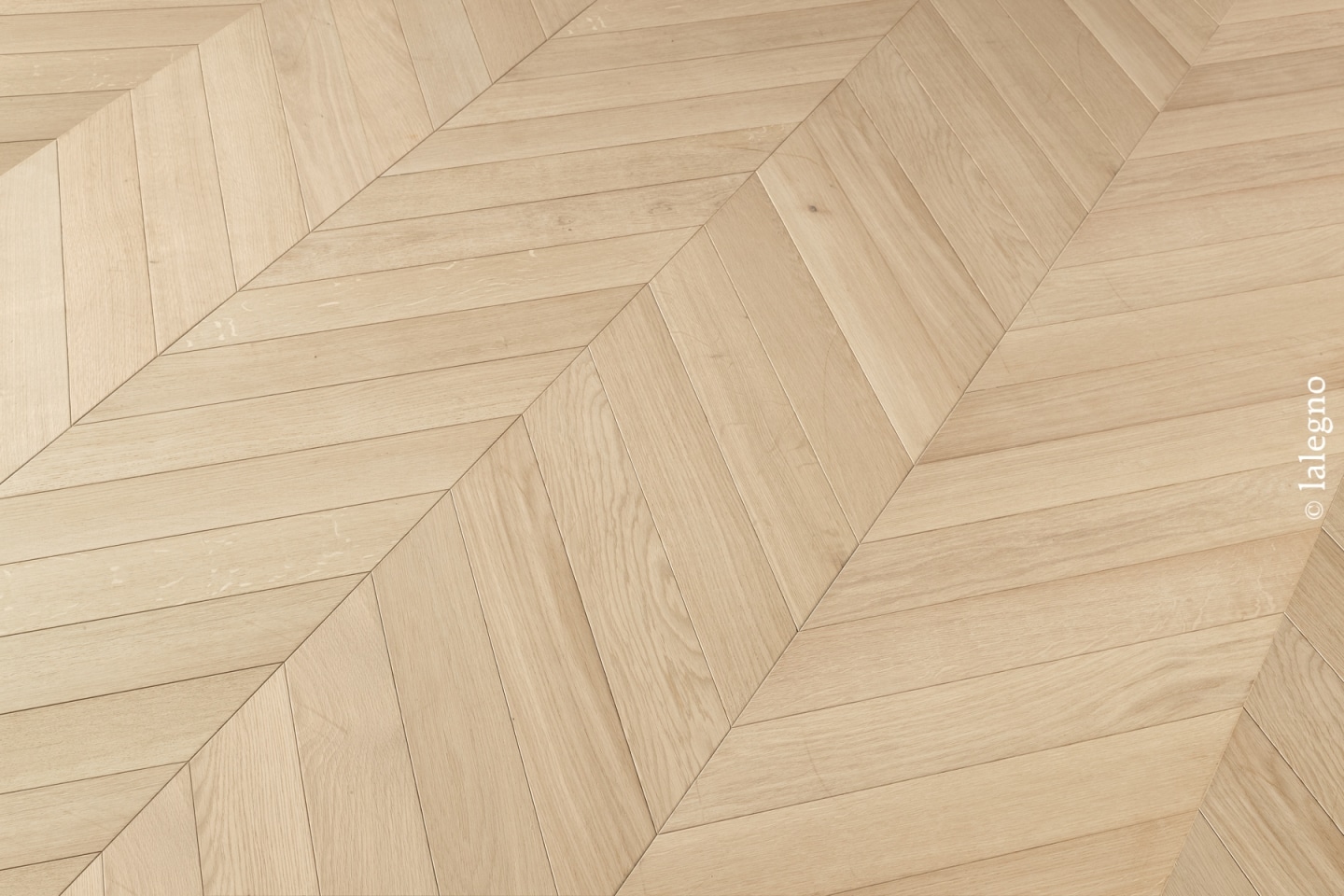 Sol en parquet chêne clair au motif chevron élégant. Détail des lames de bois naturel.