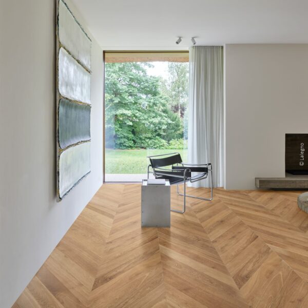 Fauteuil design et tableau abstrait dans un salon moderne. Parquet chevron en chêne Lalegno, baie vitrée avec vue sur jardin.