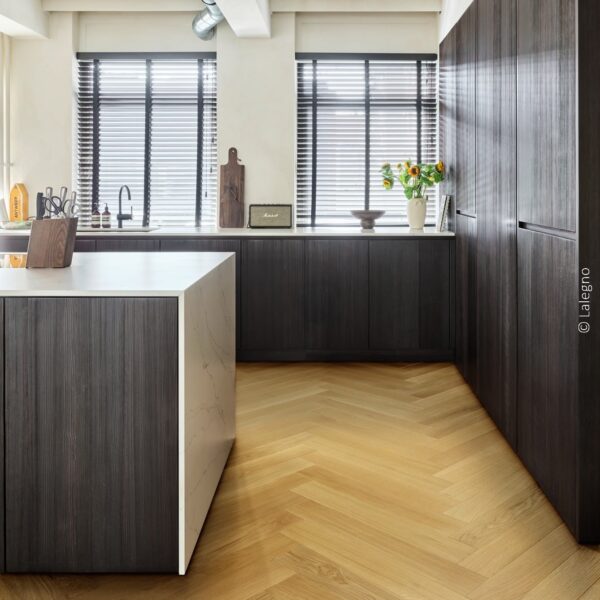 Cuisine industrielle chic: armoires bois foncé, îlot marbre blanc, parquet chêne clair à chevrons. Éclairage sur rail.