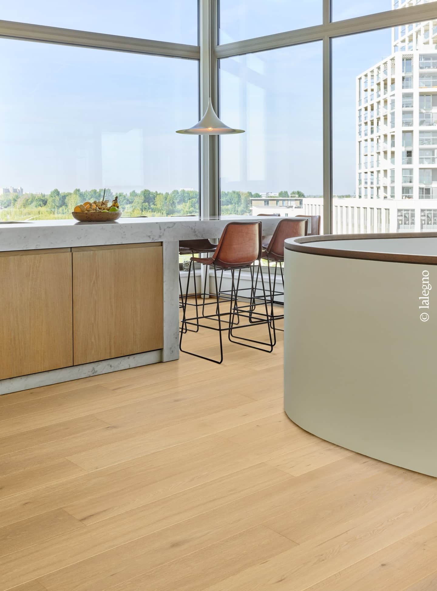 Plancher en chêne clair dans cuisine de luxe. Îlot en marbre, tabourets en cuir, et vue panoramique urbaine. Design élégant. © lalegno